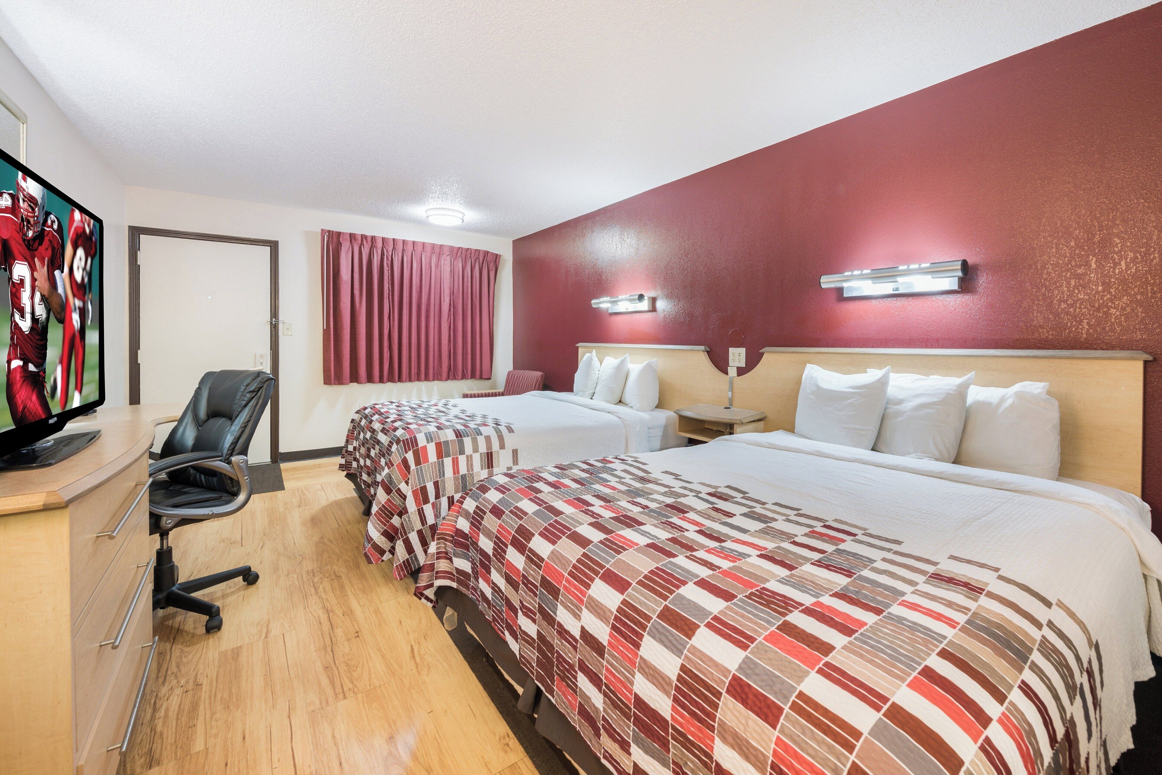 Une chambre d’hôtel avec deux lits, un bureau équipé d’un ordinateur, une chaise et un téléviseur fixé au mur.