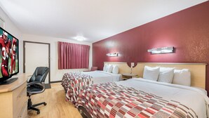 Quarto de hotel com duas camas, uma mesa de escritório com computador, uma cadeira e televisão na parede.