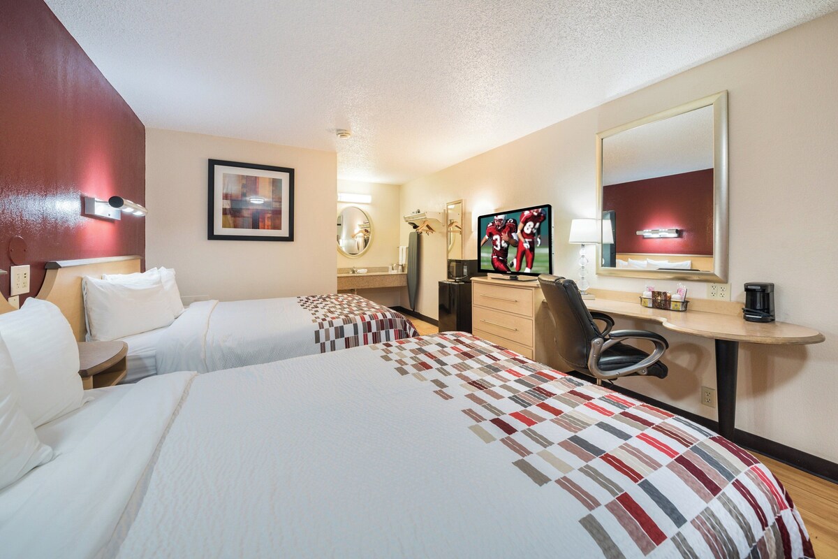 A hotel room with two beds, a desk with a computer, a chair, a mirror, and a TV.