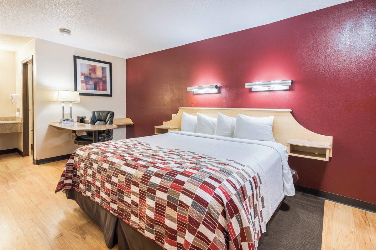 A hotel room with a bed, a desk, a chair, a lamp, and a painting on the wall.