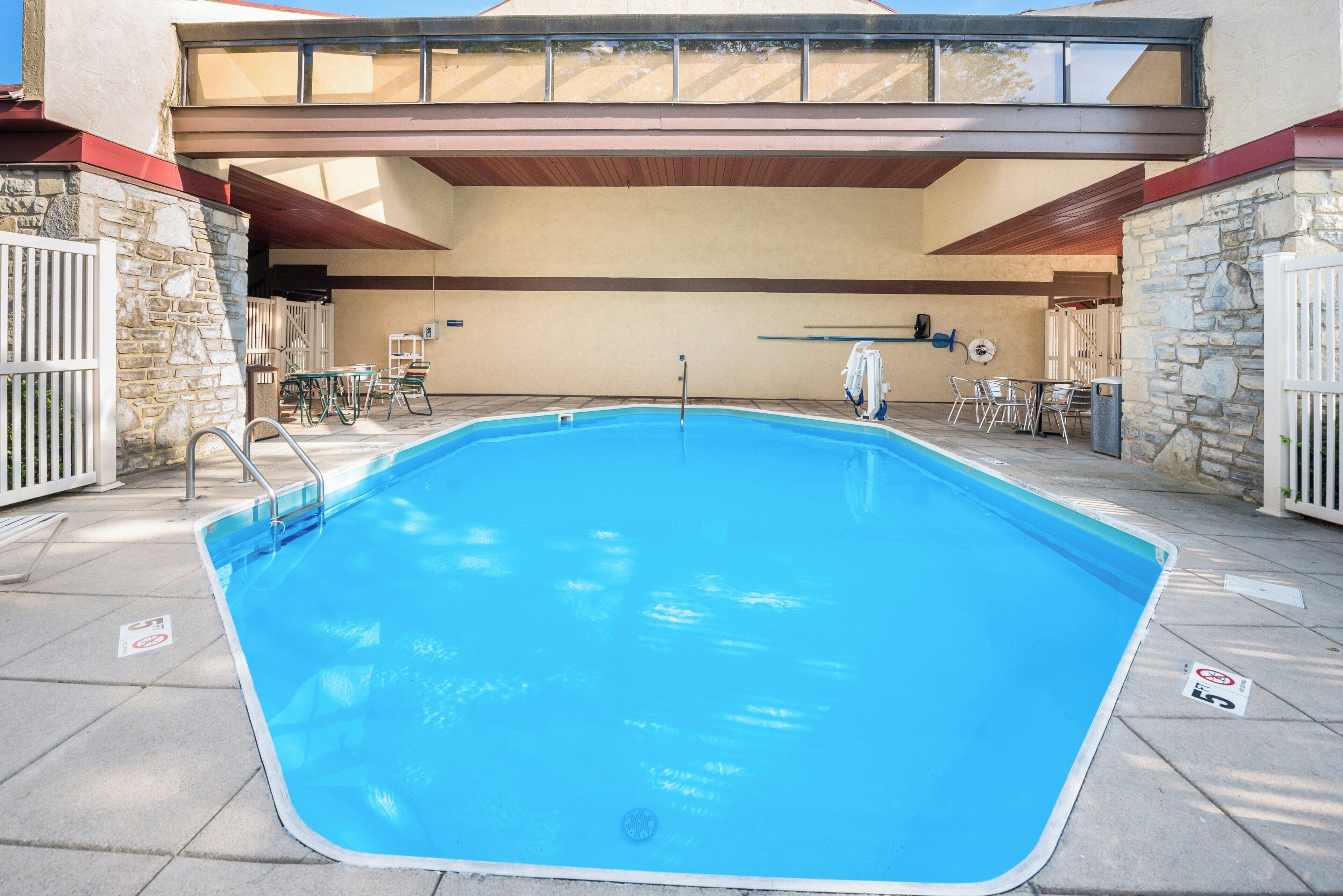 A swimming pool with a diving board, surrounded by stone walls and a covered patio area.