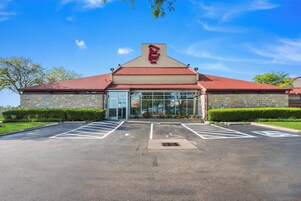 Un Red Roof Inn con fachada de piedra, techo rojo y estacionamiento con espacios para discapacitados.