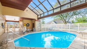 An indoor swimming pool with a clear view of the sky through large windows, a stone wall, and a white fence surrounding the area.
