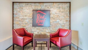 A Red Roof Inn lobby with a stone wall, two red leather chairs, and a wooden table.