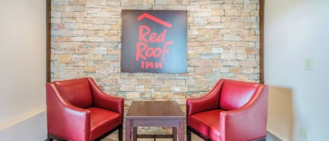 Lobby de um Red Roof Inn, com parede de pedra, duas poltronas de couro vermelho e uma mesa de madeira.
