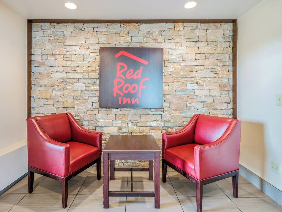 Vestíbulo de Red Roof Inn con pared de piedra, dos sillones de cuero rojo y una mesa de madera.