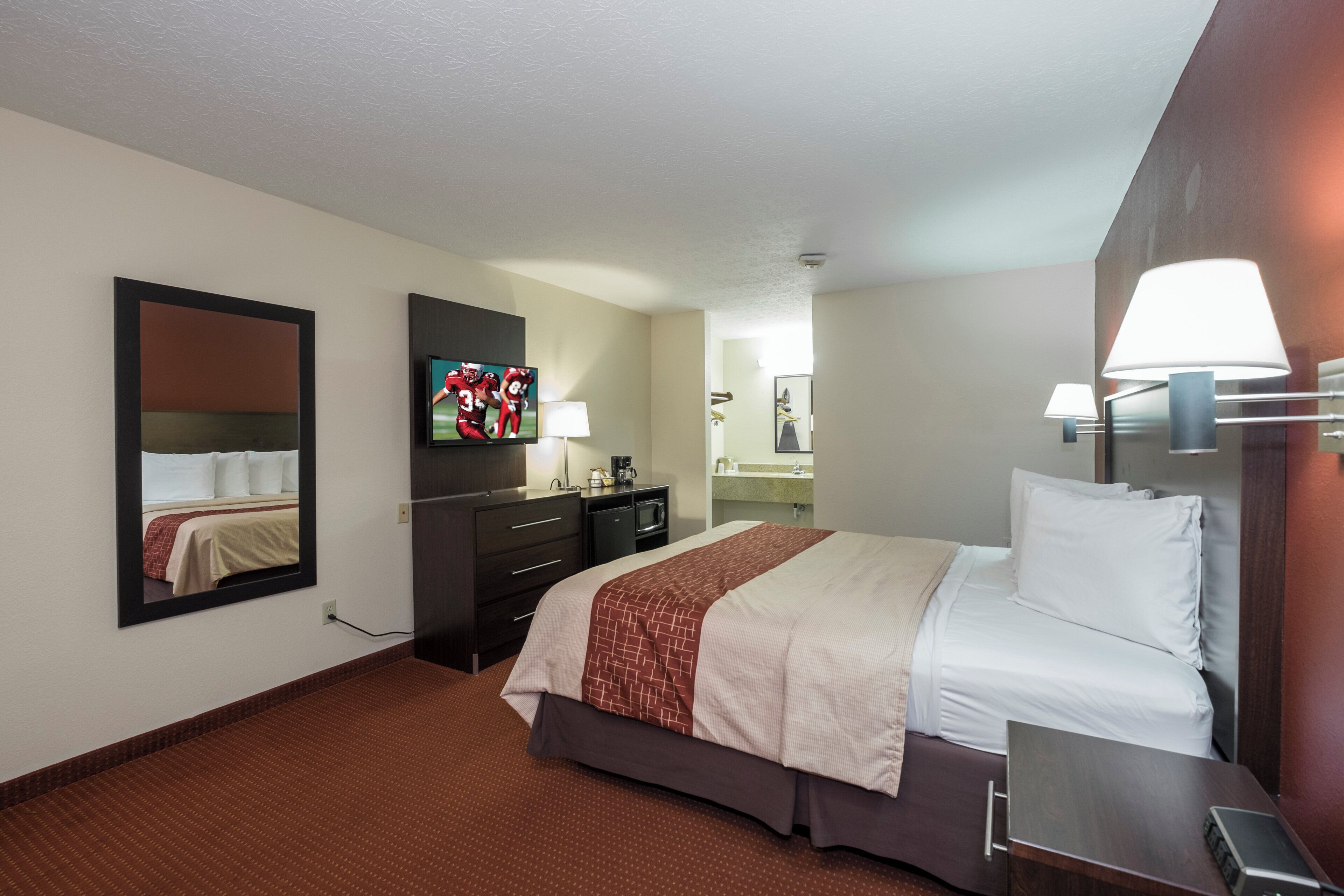A hotel room with a bed, a television, a dresser, a mirror, and a lamp.