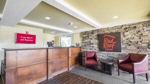 Zona de recepción con un escritorio de madera, dos sillones de cuero, una pared de piedra y el letrero de Red Roof Inn.