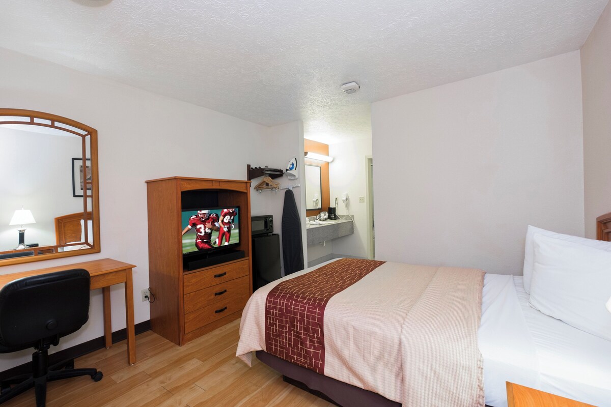 A hotel room with a wooden desk, a TV, a bed with a patterned blanket, and a mirror.
