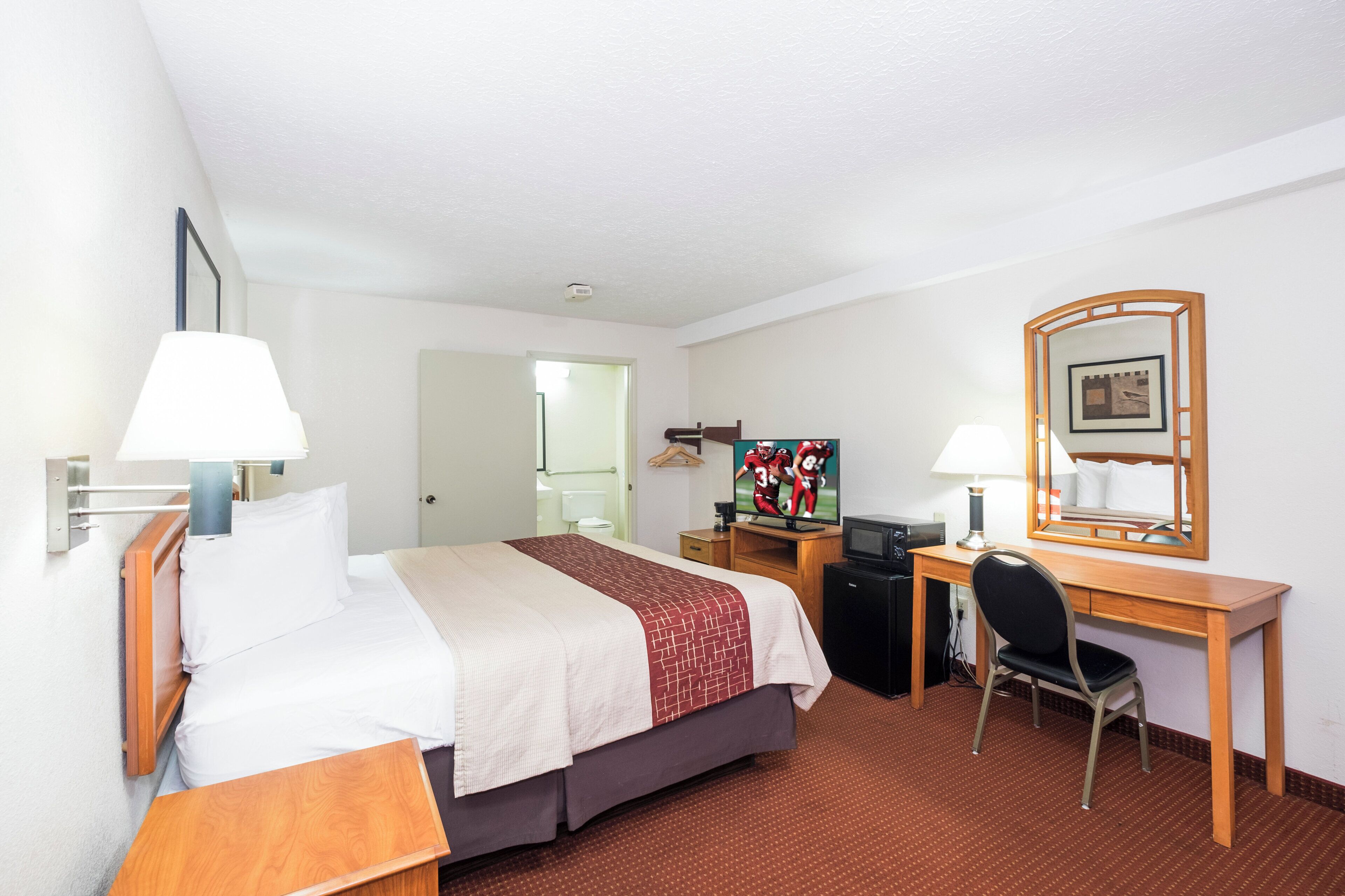 A hotel room with a bed, desk, chair, and a television.