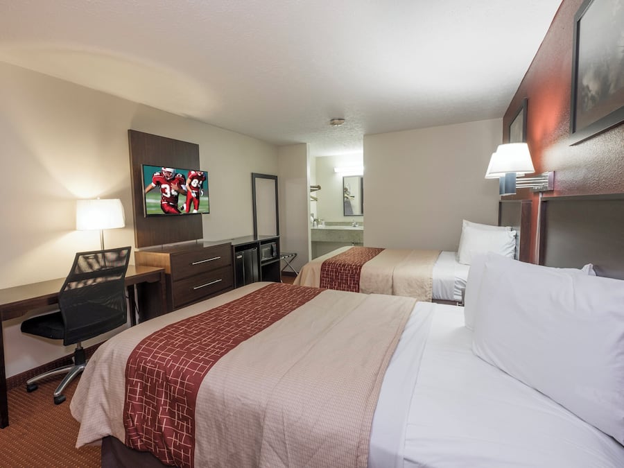 A hotel room with two beds, a desk, a chair, a television, and a mirror.