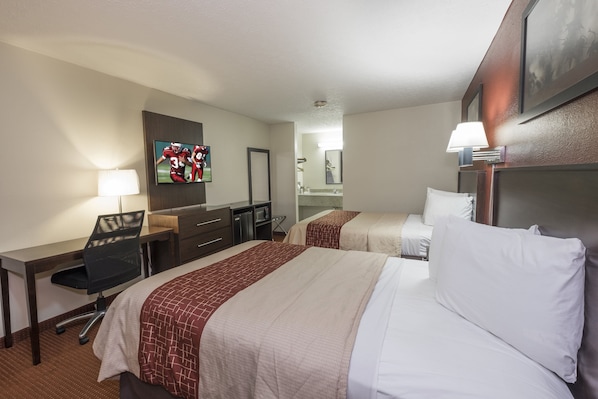 A hotel room with two beds, a desk, a chair, a TV, and a bathroom visible through an open door.