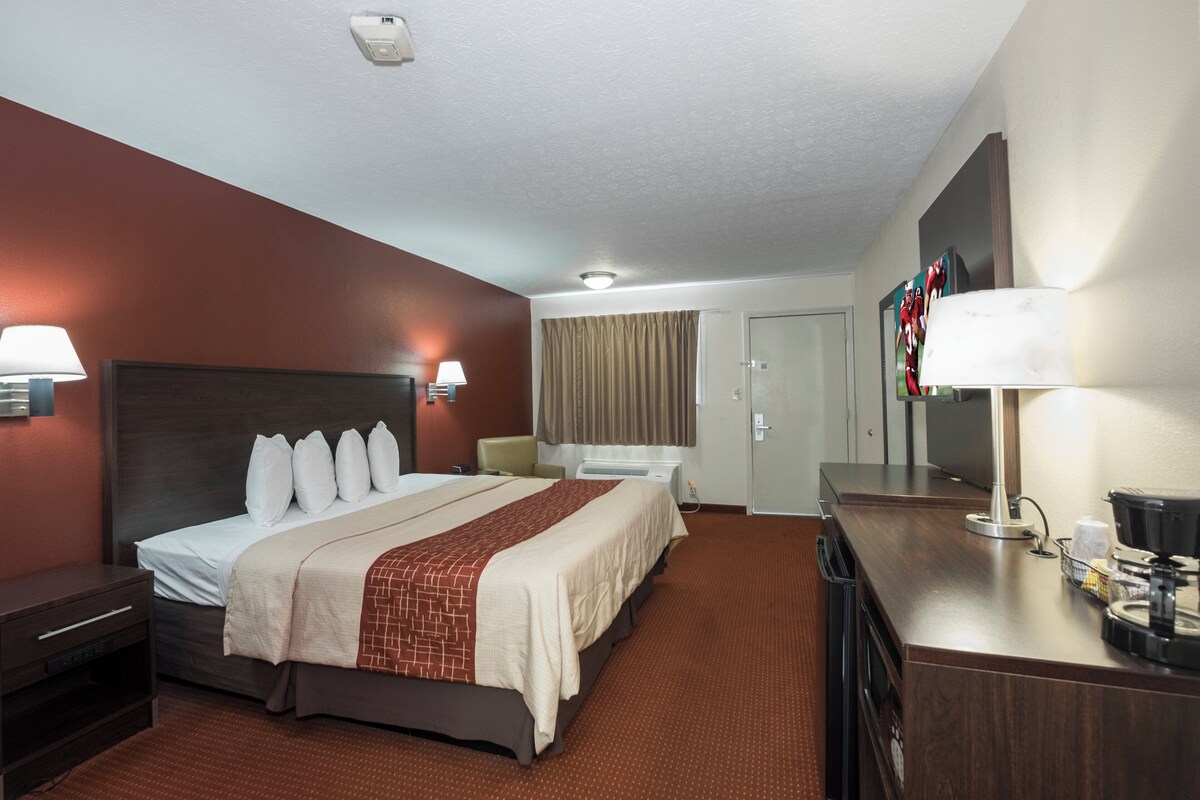 A hotel room with a large bed, a desk with a coffee maker, a TV, and a bathroom with a shower and toilet.