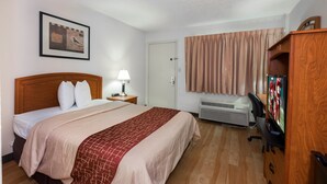 A hotel room with a bed, a desk with a computer, an air conditioner, a lamp, and a framed picture on the wall. - Red Roof Inn Columbus Northeast - Westerville (Westerville)
