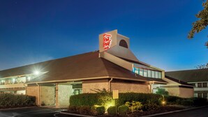 Un Red Roof Inn con un diseño arquitectónico moderno, que destaca un letrero rojo y blanco prominente, un estacionamiento y jardines bien cuidados.
