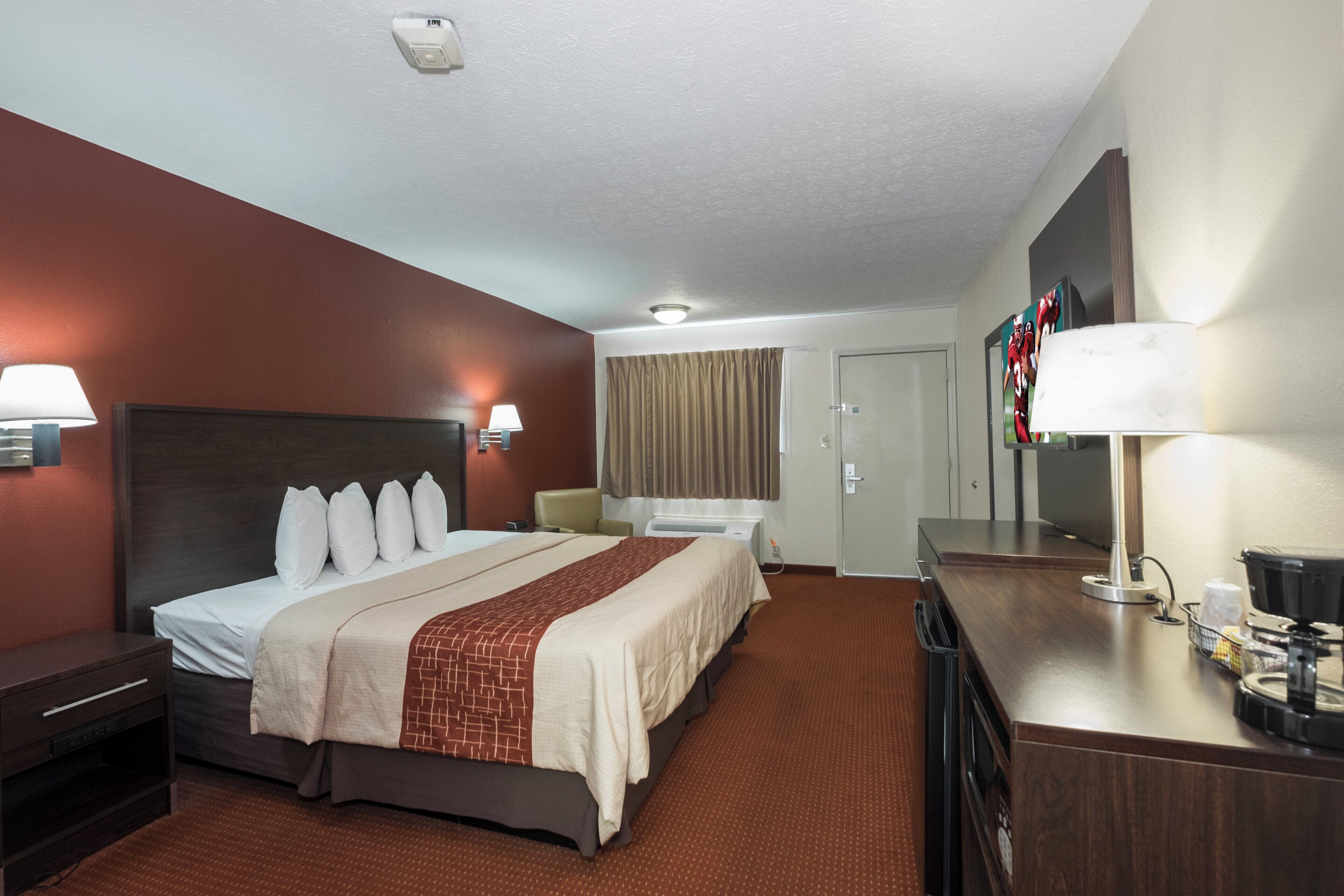 A hotel room with a large bed, bedside lamps, a desk with a lamp, a television, and a door.