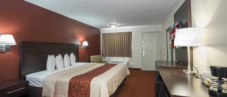A hotel room with a large bed, bedside lamps, a desk with a lamp, a television, and a door.