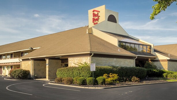 Un Red Roof Inn con un letrero rojo llamativo, fachada de piedra y estacionamiento.