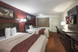 A hotel room with two beds, a desk, a television, and a window with curtains.