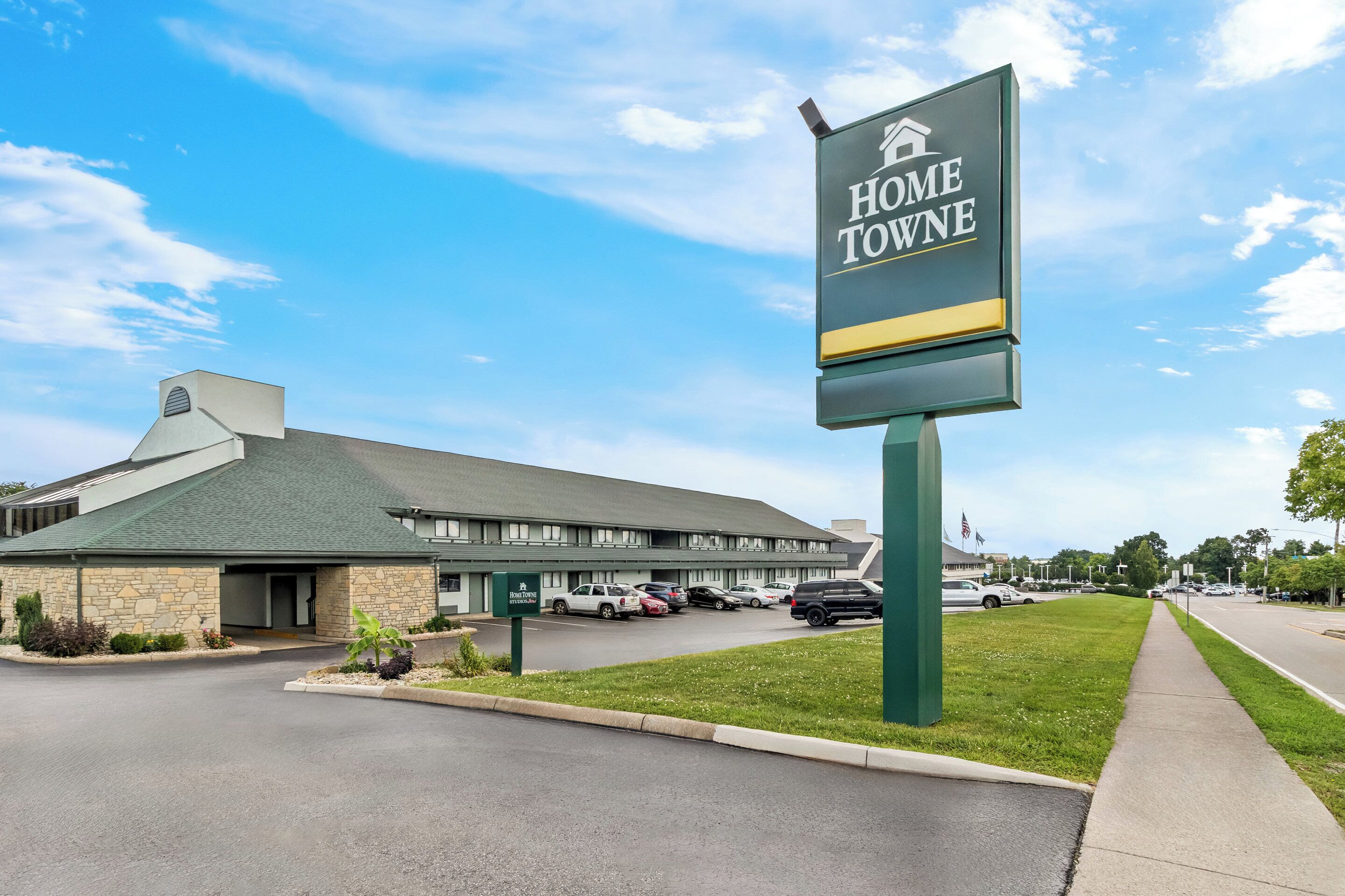 Um hotel chamado "Home Towne", com fachada de pedra, telhado verde e estacionamento com vários carros.