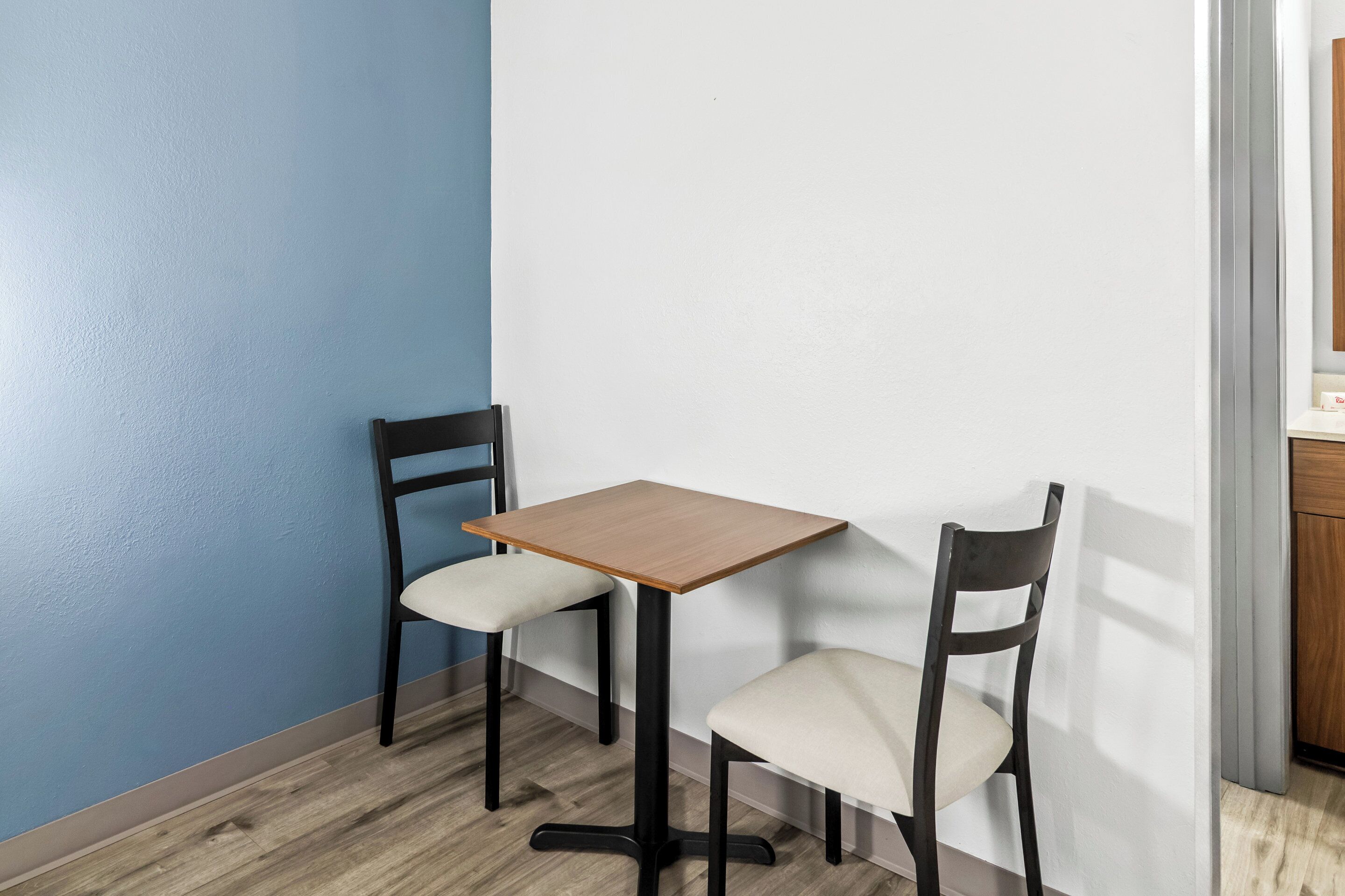 Um espaço de refeições pequeno com uma mesa de madeira e duas cadeiras, uma parede azul e um armário de madeira.
