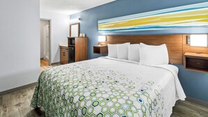Een hotelkamer met een groot bed, een houten hoofdeinde, een nachtkastje, een dressoir en een groot abstract schilderij aan de muur.