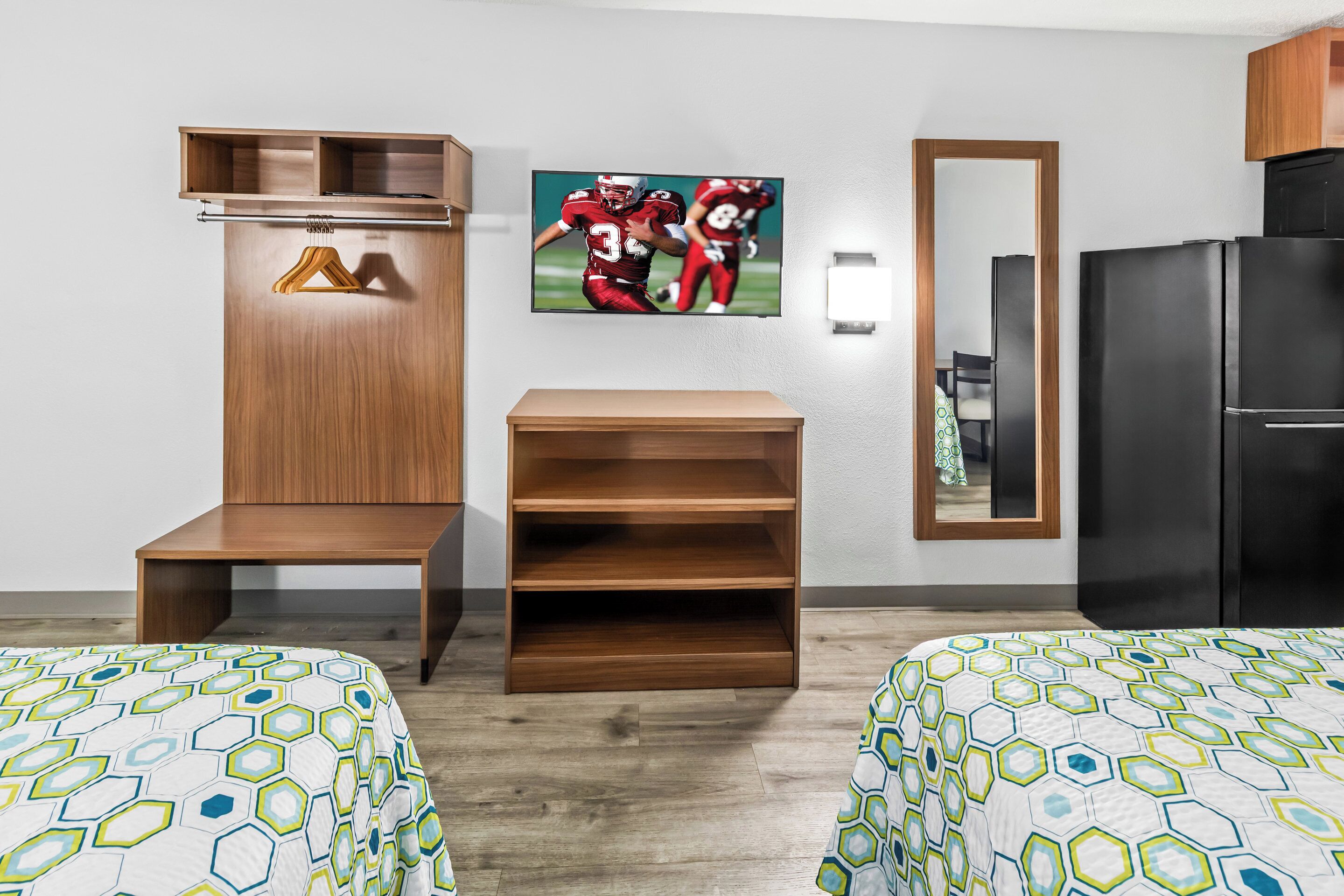 A hotel room with two beds, a wooden wardrobe, a mirror, and a television displaying a football game.