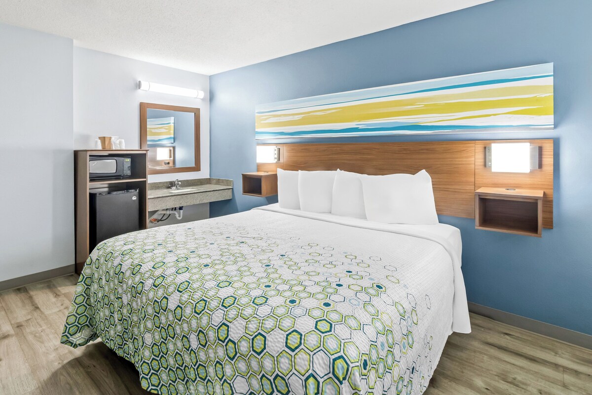 Habitación de hotel con una cama grande, cabecera de madera, televisor montado en la pared, escritorio con computadora y zona de baño.