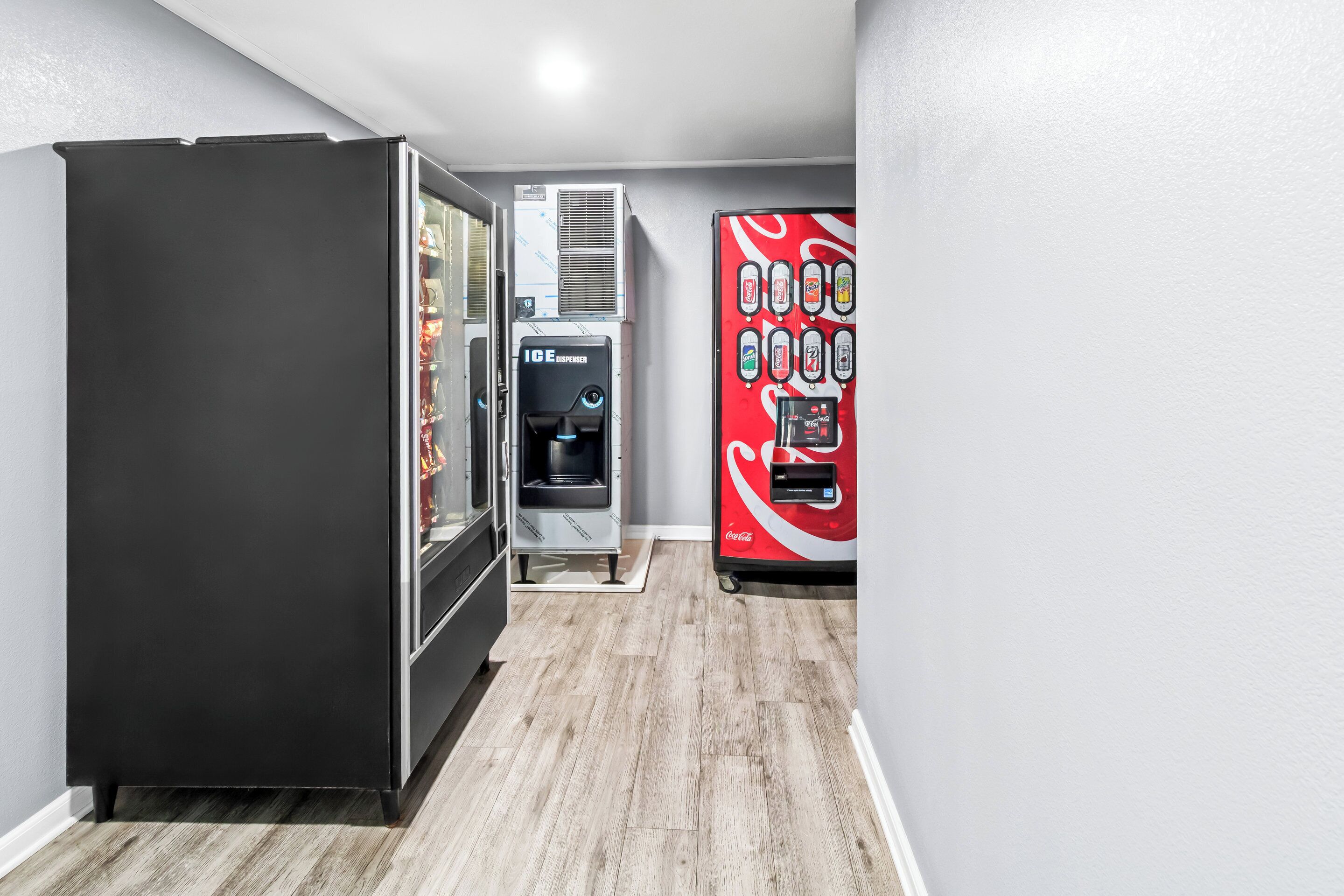 Un couloir avec un réfrigérateur noir, un distributeur de boissons et un distributeur automatique de Coca-Cola.