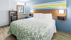 Een hotelkamer met een groot bed, een houten hoofdbord, een tv aan de muur, een bureau met een computer en een badkamergedeelte.