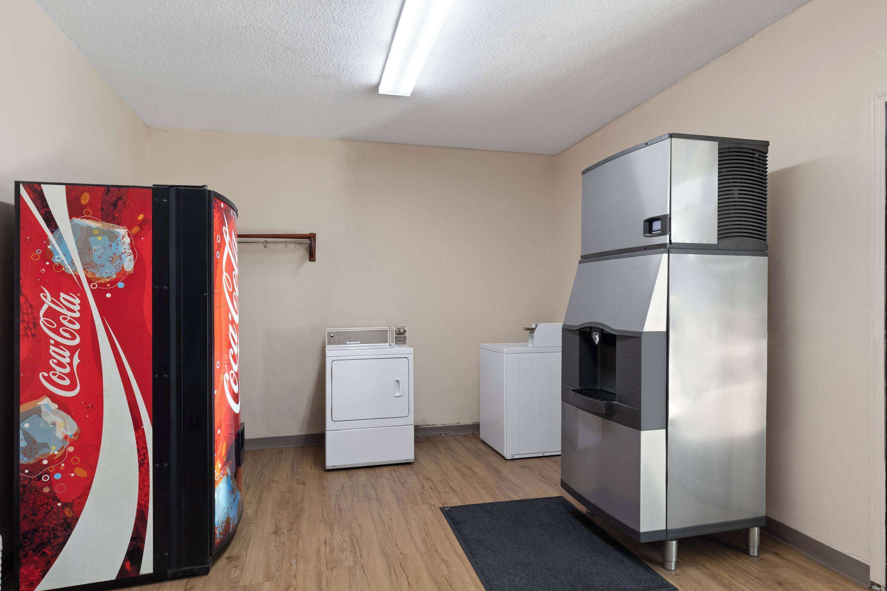 A compact hotel room with a refrigerator, a washing machine, and a Coca-Cola vending machine.