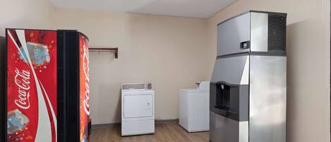 A compact hotel room with a refrigerator, a washing machine, and a Coca-Cola vending machine.