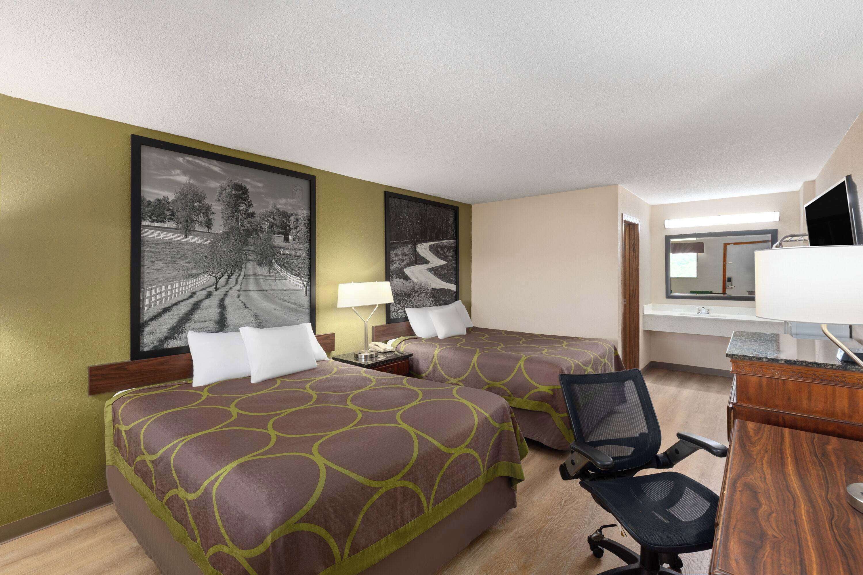 Quarto de hotel com duas camas, uma escrivaninha, uma cadeira e uma televisão.