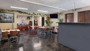 A restaurant with a bar area, multiple tables and chairs, and a kitchen in the background. - Super 8 by Wyndham Fort Mitchell Cincinnati Area (Fort Mitchell)