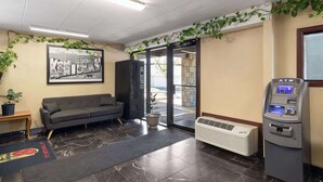A lobby with a sofa, a framed welcome sign, an ATM, and a door leading outside. - Super 8 by Wyndham Fort Mitchell Cincinnati Area (Fort Mitchell)