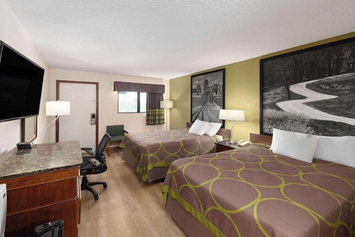 A hotel room with two beds, a desk, a TV, and a large painting on the wall.