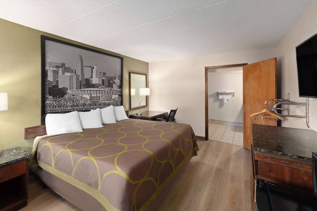A hotel room with a large bed, a desk, a chair, a TV, and a bathroom.