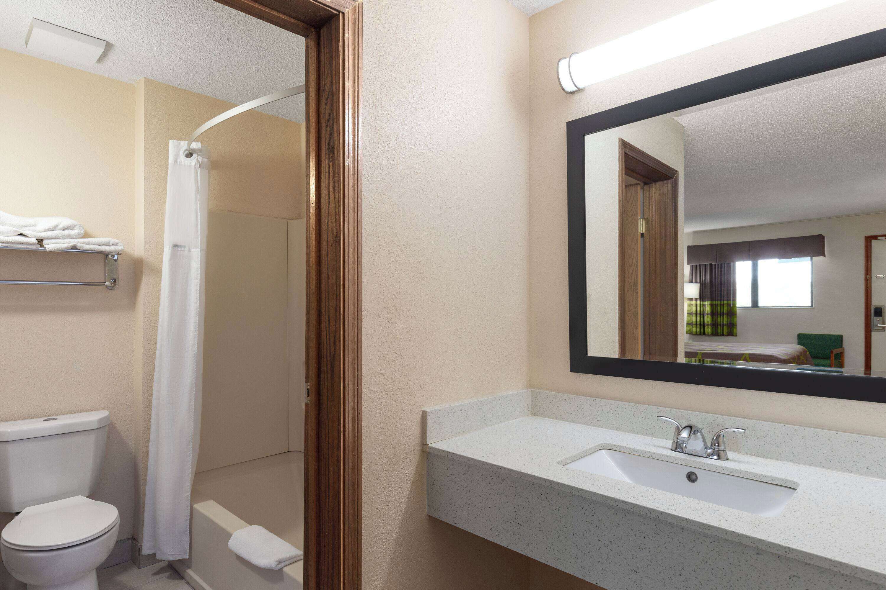 A bathroom with a toilet, shower, sink, and a large mirror.