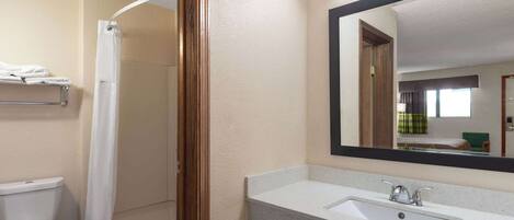 A bathroom with a toilet, shower, sink, and a large mirror.