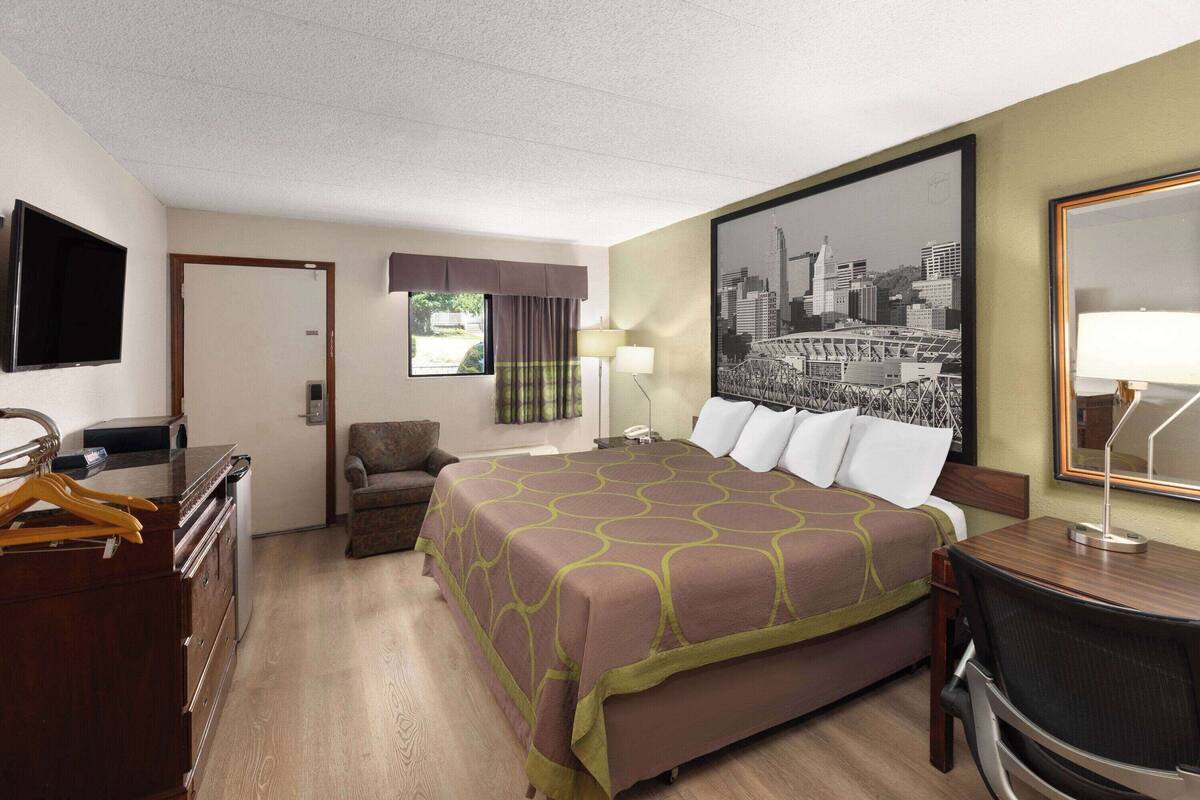 A hotel room with a bed, a desk, a chair, a TV, and a window with curtains.