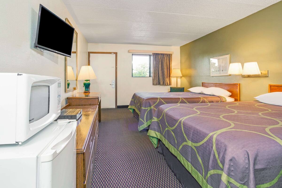 A hotel room with two beds, a television, a microwave, and a window with curtains.