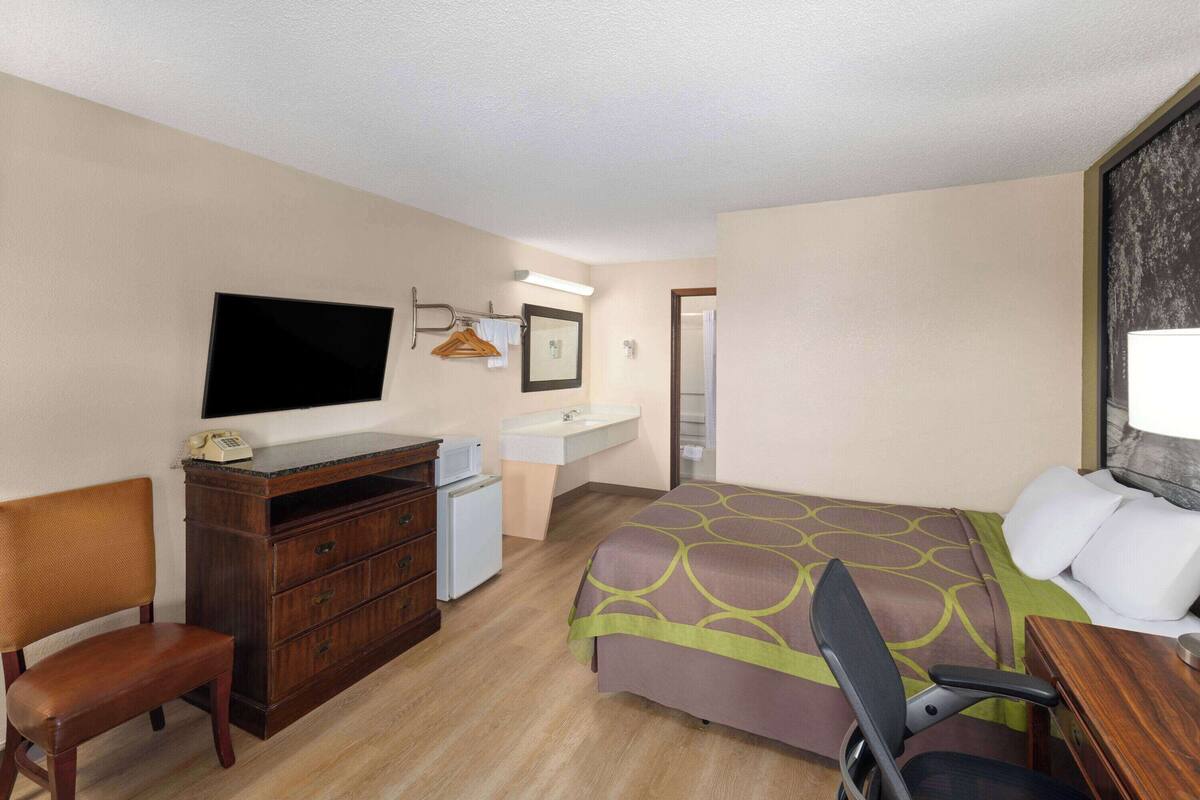 A hotel room with a bed, a desk, a chair, a dresser, a television, a sink, and a mirror.