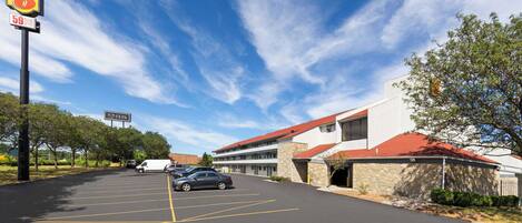 Un parking avec une enseigne Super 8, un bâtiment avec un toit rouge et un ciel bleu dégagé.