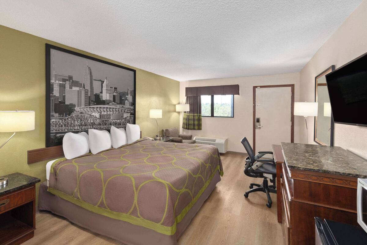 A hotel room with a large bed, a desk, a chair, a television, and a window with curtains.
