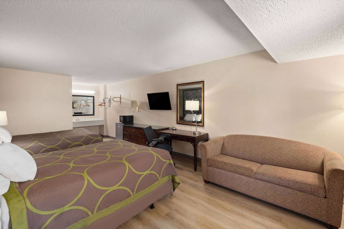 A hotel room with two beds, a desk, a chair, a sofa, a TV, and a mirror.