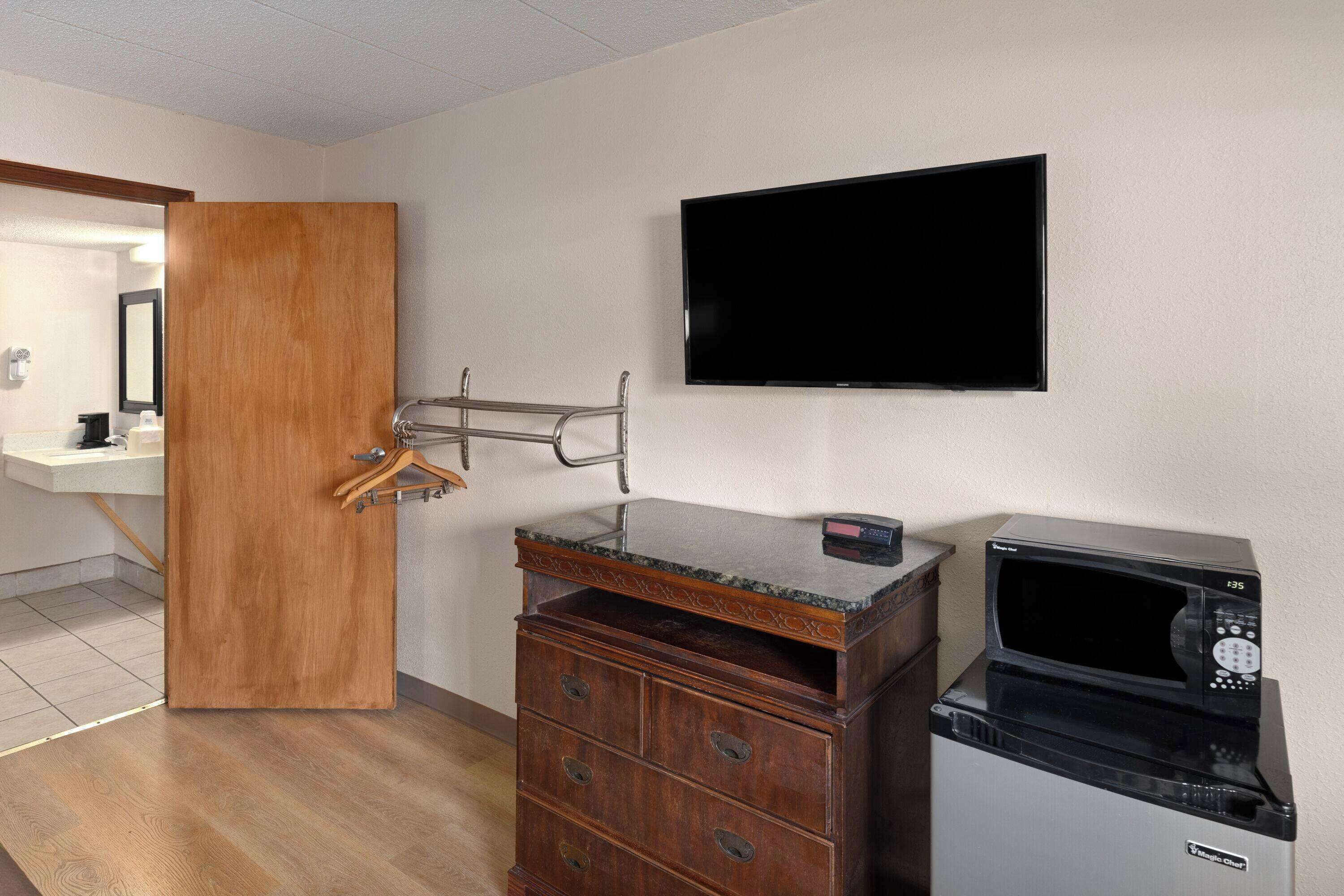 A hotel room with a wooden dresser, a microwave, a flat-screen TV, and a wooden door.