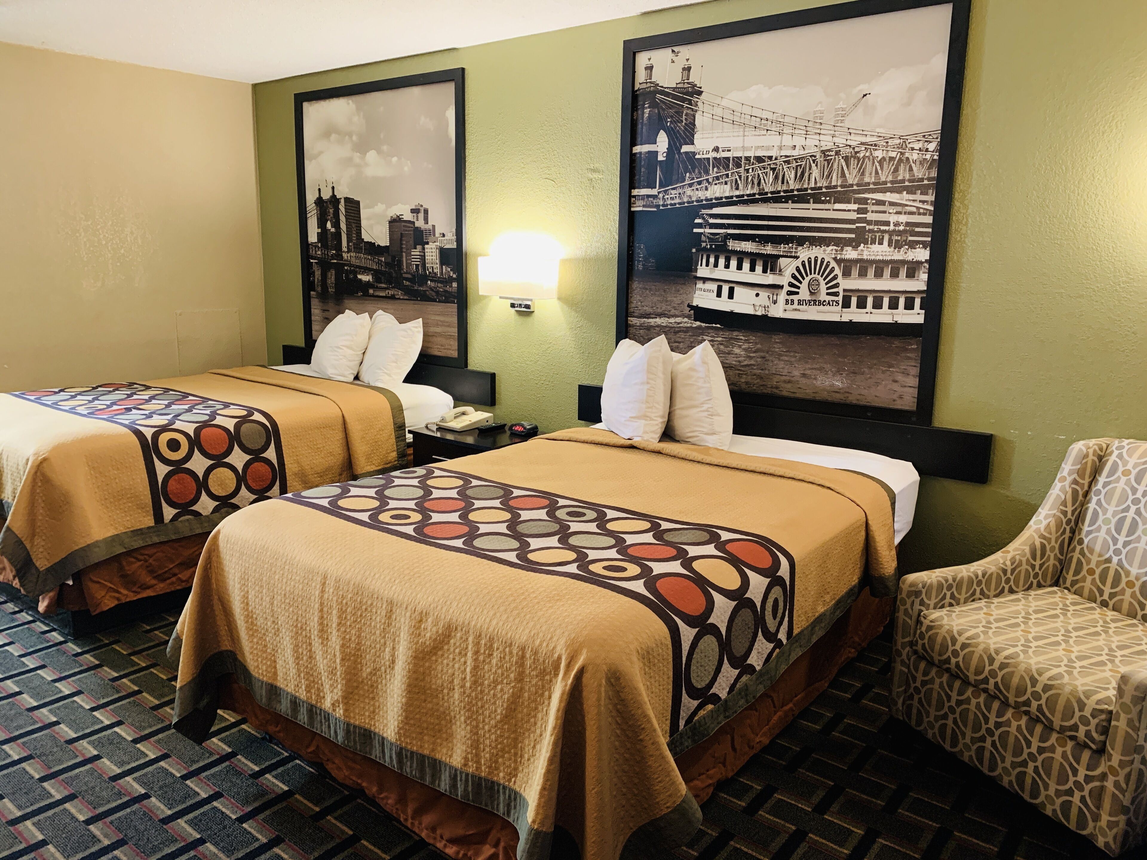 Habitación de hotel con dos camas, una silla y una pared decorada con dos cuadros.