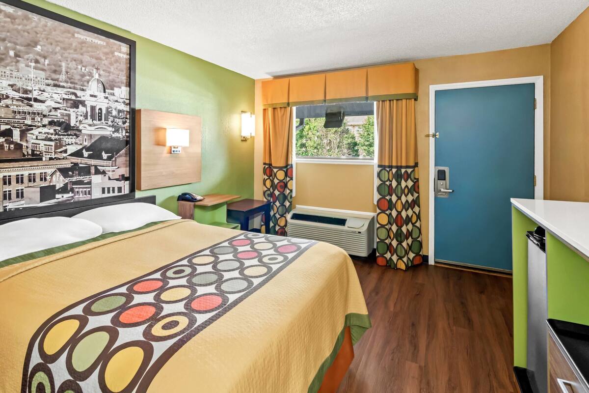 A hotel room with a bed, a desk, a window with curtains, a radiator, and a door.
