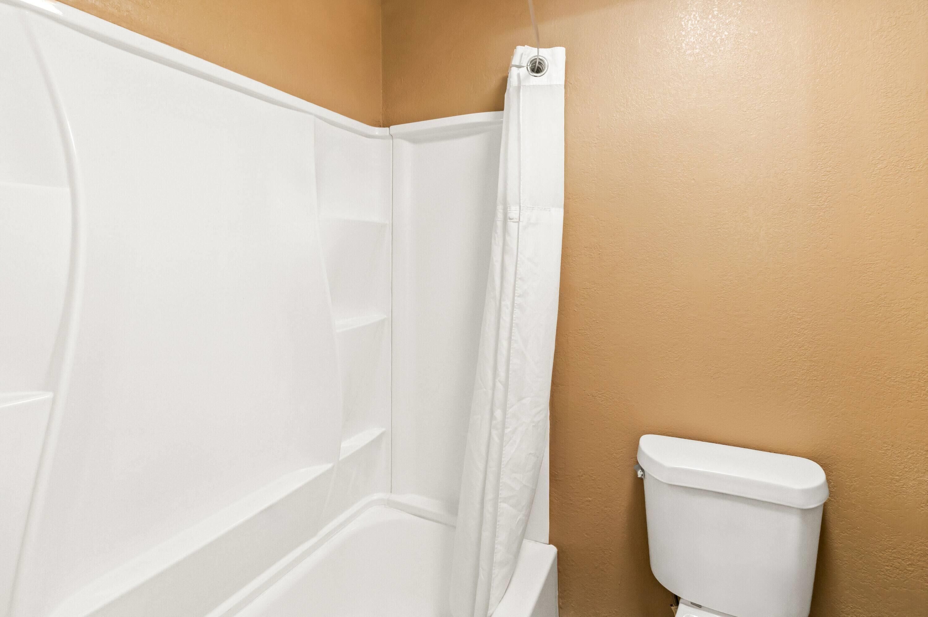 A corner of a bathroom with a white bathtub, a white toilet, and a beige wall.
