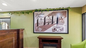 A reception area with a framed welcome sign, a wooden reception desk, a fireplace, and a green couch. - Super 8 by Wyndham Cincinnati/Springdale OH (Cincinnati)